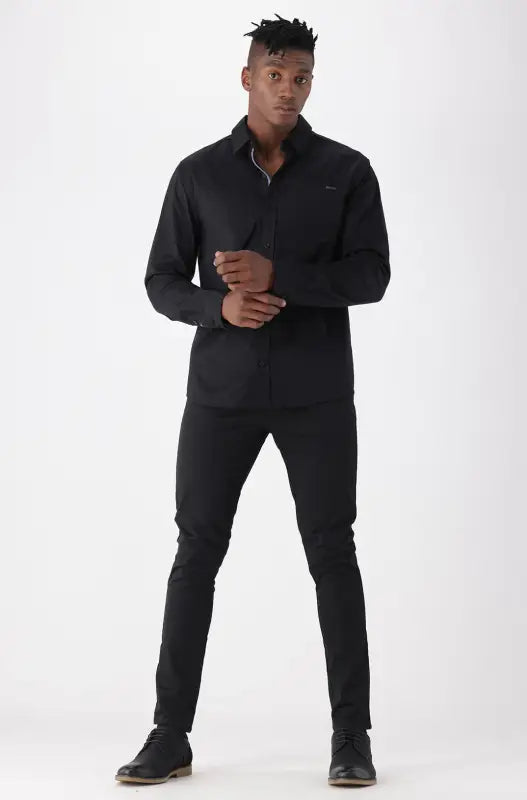 A men’s black long-sleeved collared shirt and black pants with black shoes.