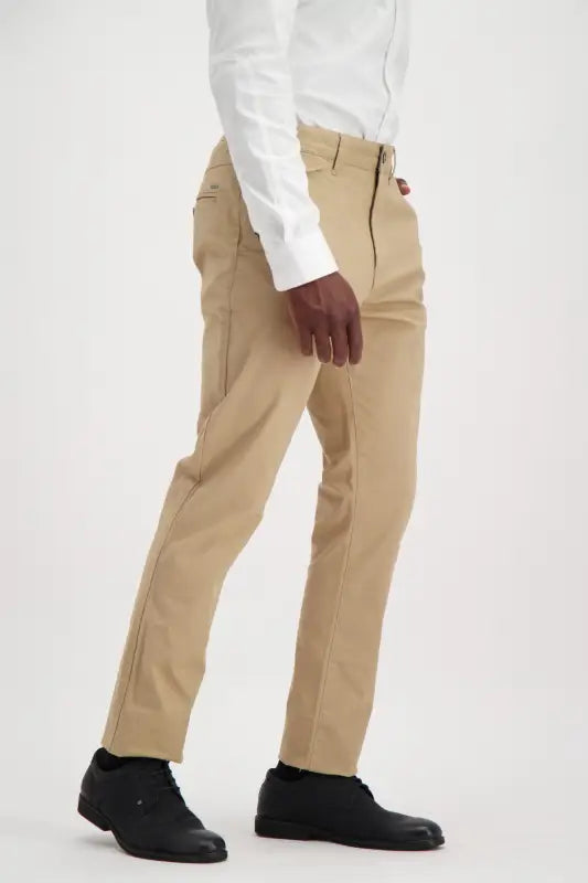 Men’s tan chino pants with a white button-up shirt and black shoes.