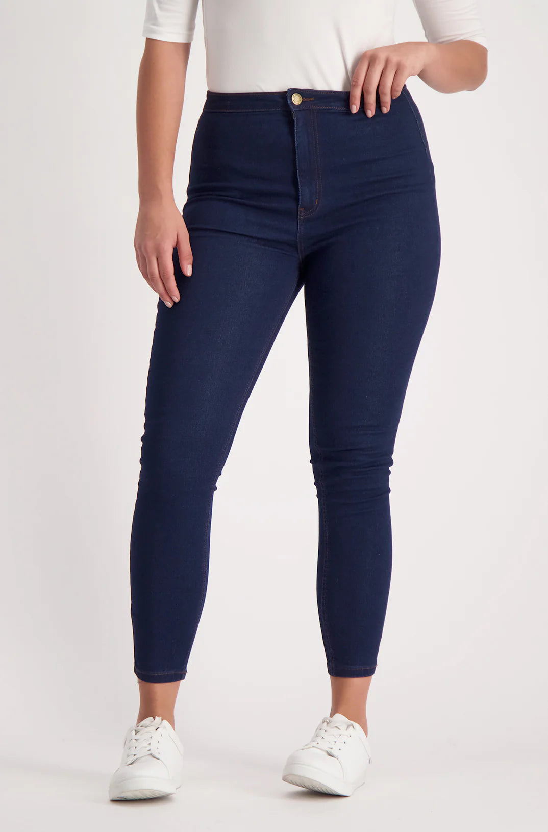 A woman wearing dark blue high-waisted skinny jeans with a single gold button closure.
