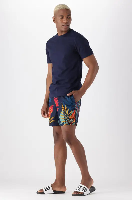 Men’s navy blue t-shirt and floral swim shorts with slides.