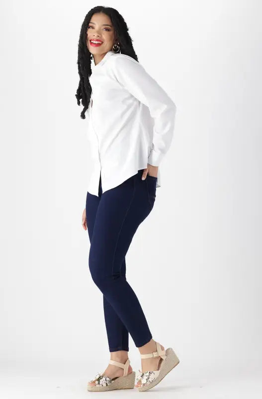 A woman’s white long-sleeved button-up shirt paired with dark blue skinny jeans and floral-adorned beige wedge sandals.