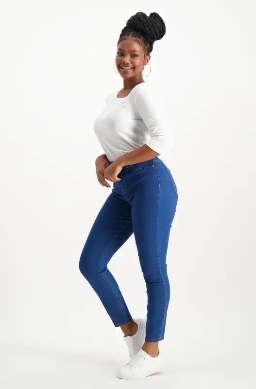 Women’s white long-sleeved top and blue skinny jeans with white sneakers.