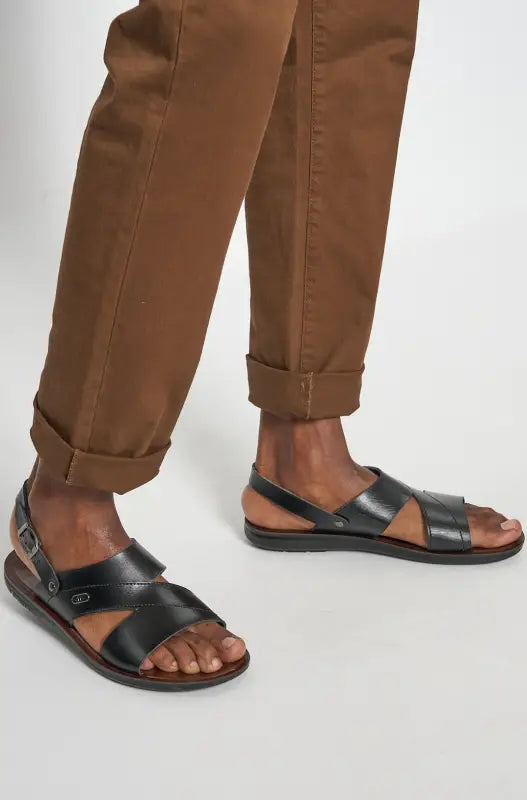 Men’s black leather sandals with brown pants.