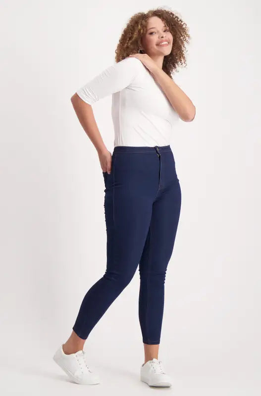 Woman in a white short-sleeved top, dark blue skinny jeans, and white sneakers