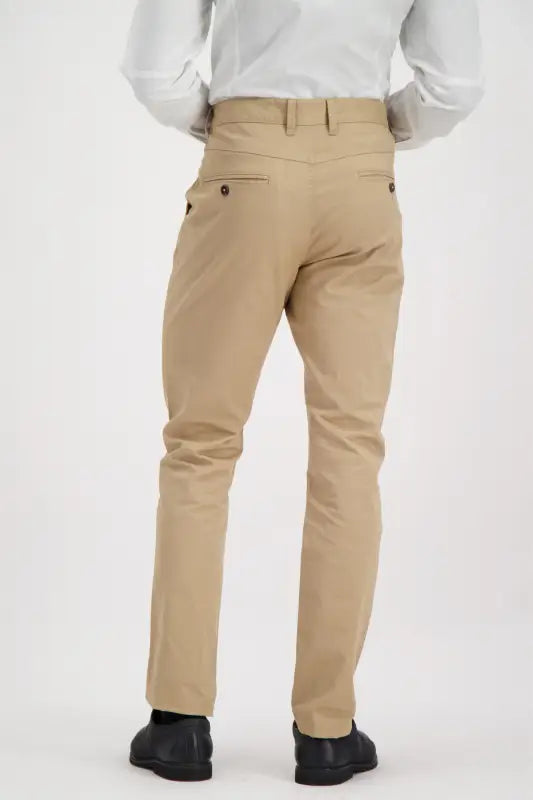 Men’s tan slim-fit dress pants with dark buttons on the back pockets.