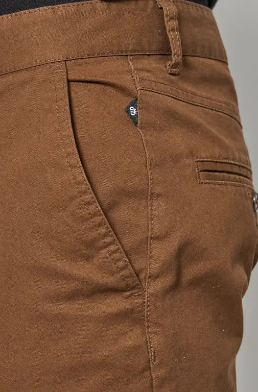 Close-up of brown cotton trousers with a pocket and belt loop.