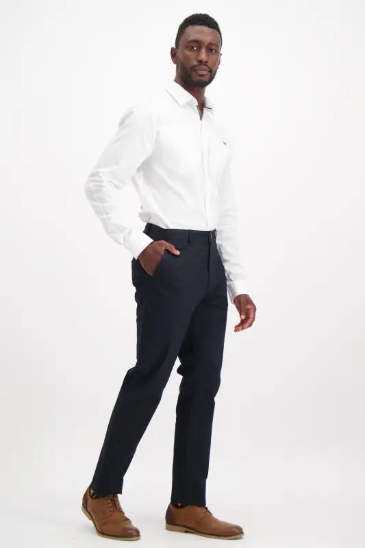 Men’s white long-sleeved dress shirt with dark blue trousers and brown leather shoes.