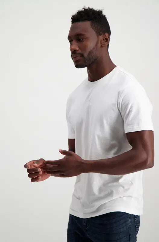 A man wearing a white crew neck t-shirt and dark blue jeans.