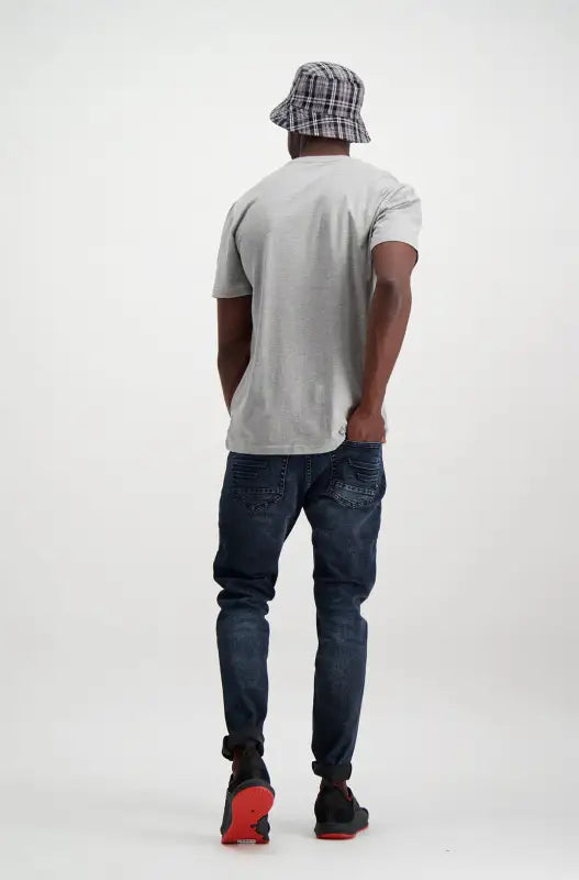 A person wearing a light grey t-shirt, dark blue distressed jeans, and a grey plaid bucket hat.