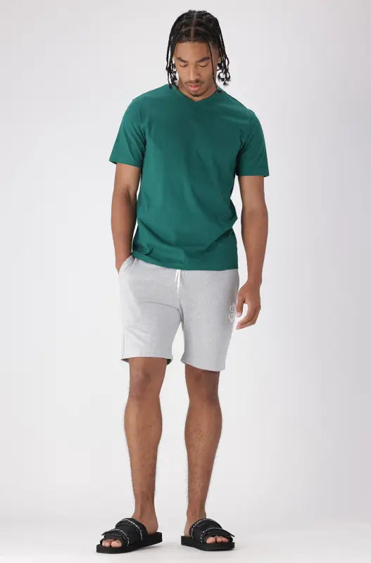 Men’s teal V-neck t-shirt with light grey athletic shorts and black slide sandals.