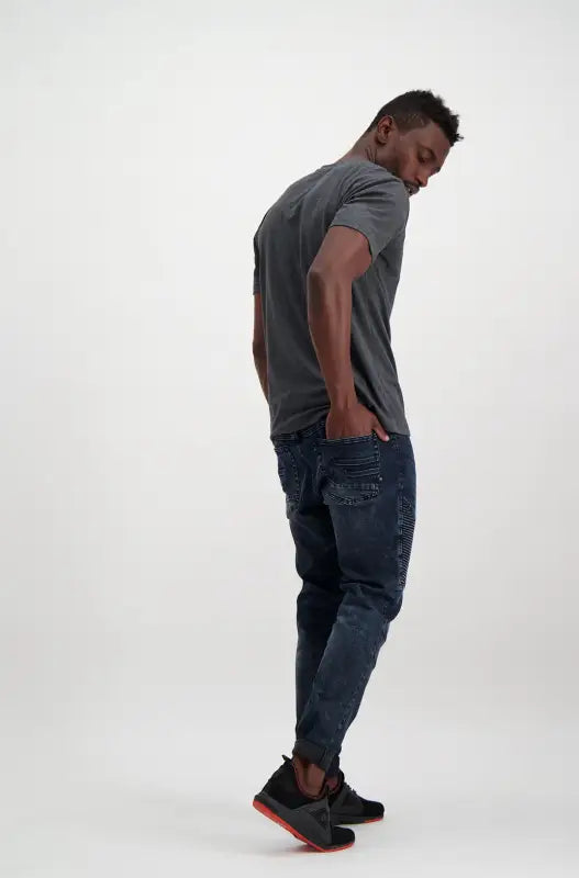 Men’s dark grey t-shirt, distressed dark blue jogger jeans, and black and orange athletic shoes.