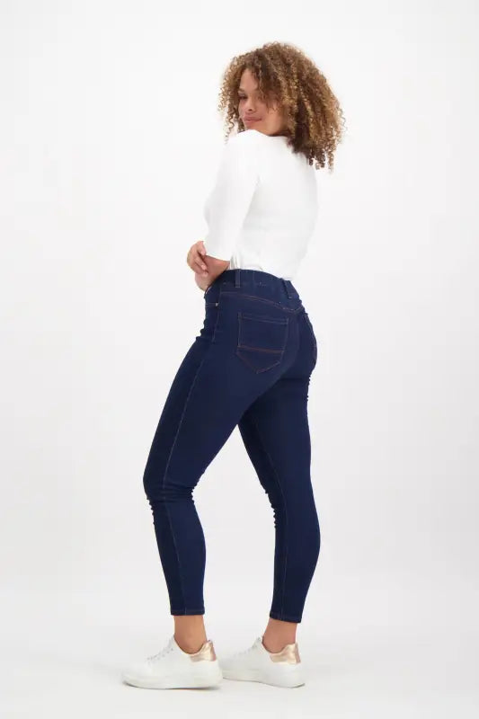 A woman wearing dark blue skinny jeans and a white short-sleeved top.