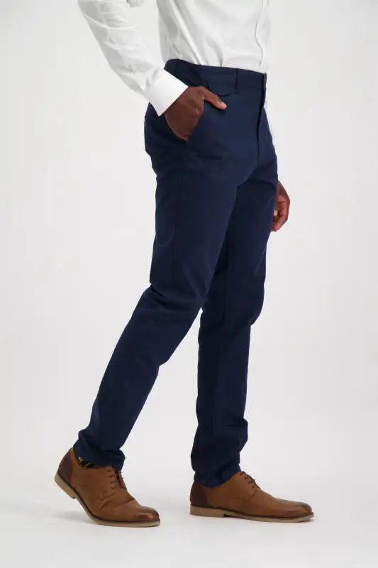 Men’s navy blue slim-fit trousers with a white button-up shirt and brown dress shoes.